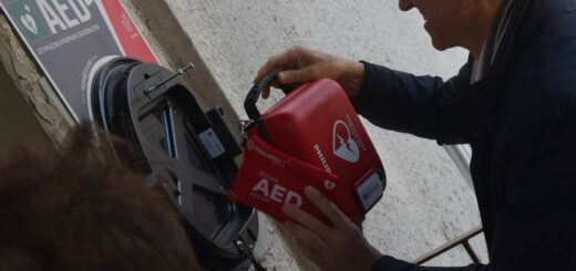 Prezydent Olsztyna Piotr Grzymowicz umieszcza czerwoną skrzynkę z przenośnym defibrylatorem na ścianie budynku szkoły.