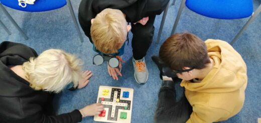 Troje uczniów siedzi na podłodze i grają w chińczyka dla niewidomych.