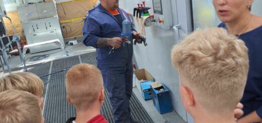 Dzieci obserwują pracę mechanika samochodowego i słuchają pani oprowadzającej ich salonie