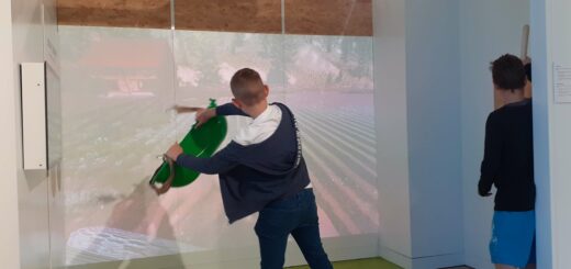 Chłopiec gra wirtualnie - stoi przed ścianą na której wyświetla się obraz z rzutnika, trzyma w ręku deskę.