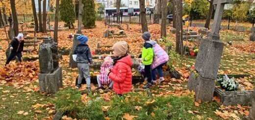 Grupka dzieci porządkuje zapomniany grób na cmentarzu na dajtkach w Olsztynie. Na grobach leży mnóstwo liści w wielu odcieniach czerwieni.