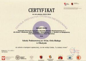 Na beżowym tle , w centralnym punkcie znajduje się fioletowy ring utożsamiający źrenicę. Na tym tle został umieszczony tekst : Certyfikat na rok szkolny 2023/2024 - Szkoła przyjazna osobom niewidomym nadany przez Kujawsko - Pomorski Ośrodek Szkolno - Wychowawczy dla Dzieci i Młodzieży Słabo Widzącej i Niewidomej nr 1 w Bydgoszczy oraz Stowarzyszenia Visus Supremus dla Szkoły Podstawowej nr 18 im. Orła Białego w Olsztynie