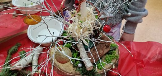 Na stole stoi stroik, który wykańcza dziecko w szarej bluzie. Obok drugie dziecko przygotowuje swój stroik świąteczny.