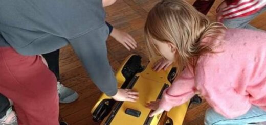 Dzieci dotykają  robota , który jest w dwóch kolorach żółtym i czarnym , robot przypomina kształtem psa..