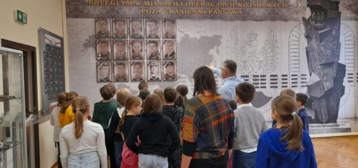 Uczniowie i ich opiekunowie wsłuchują się w opowiadanie przewodnika po terenie jednostki wojskowej