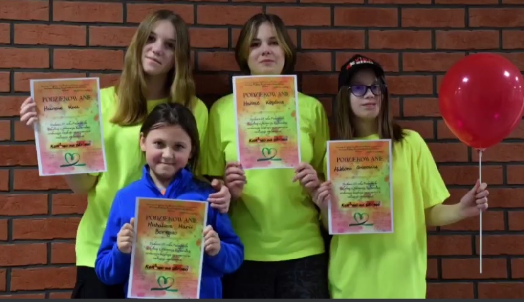 Na zdjęciu stoją cztery dziewczynki ( jedna w niebieskiej bluzie, trzy stojące za nią w zielonych koszulkach. wszystkie trzymają w rękach dyplomy , jedna z nich trzyma również czerwonego balona