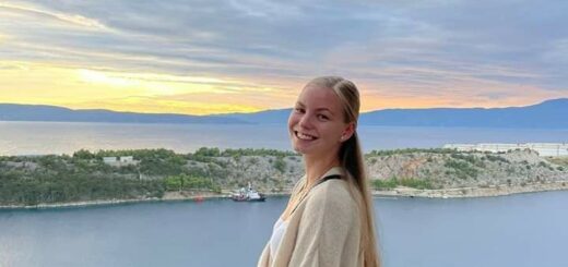 Na wzgórzu nad zatoką o zachodzie słońca stoi blondynka z długimi włosami. Na jej twarzy rysuje się uśmiech, ubrana jest w białą bluzę i jeansy.