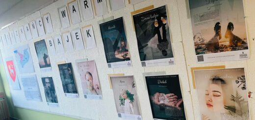 Na ścianie wiszą zdjęcia przedstawiające bohaterów bajek  warmińskich, mapa Warmii i herb Warmii . Nad nimi znajduje się napis - Mieszkańcy warmińskich bajek