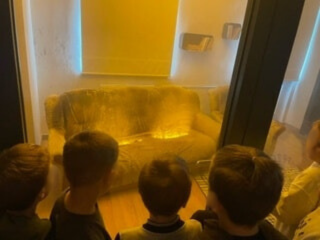 Dzieci stoją przed szybą i patrzą jak pożar trawi kanapę.