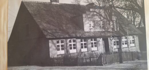 na czarno - białym zdjęciu znajduje się parterowy budynek starej szkoły, budynek jest otoczony drewnianym płotem , obok niego stoi duże drzewo