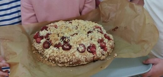 Dzieci trzymają na swoich rękach upieczone okrągłe  ciasto drożdżowe z owocami.