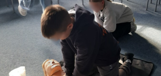 Chłopiec uczy się wykonywać sztuczne oddychanie, dziewczyna obok obserwuje jego ruchy. Za nimi idzie dziewczyna.