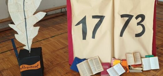 Na zdjęciu widoczny jest duży kałamarz z gęsim piórem, obok stoi wielka otwarta  księga na której kartach jest napisany rok 1773. Obok leżą w lekkim nieładzie małe książki.