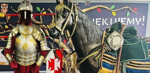 Na zdjęciu widoczna jest zbroja husarza srebrno - złota i bordowym ubraniem a także hełm. Obok zbroi stoi czarna figura konia również osiodłanego wg wzorców z epoki.