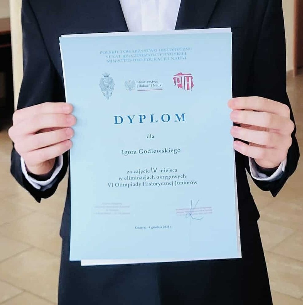 Uczeń trzyma w rękach dyplom za zdobycie 4 miejsca w konkursie