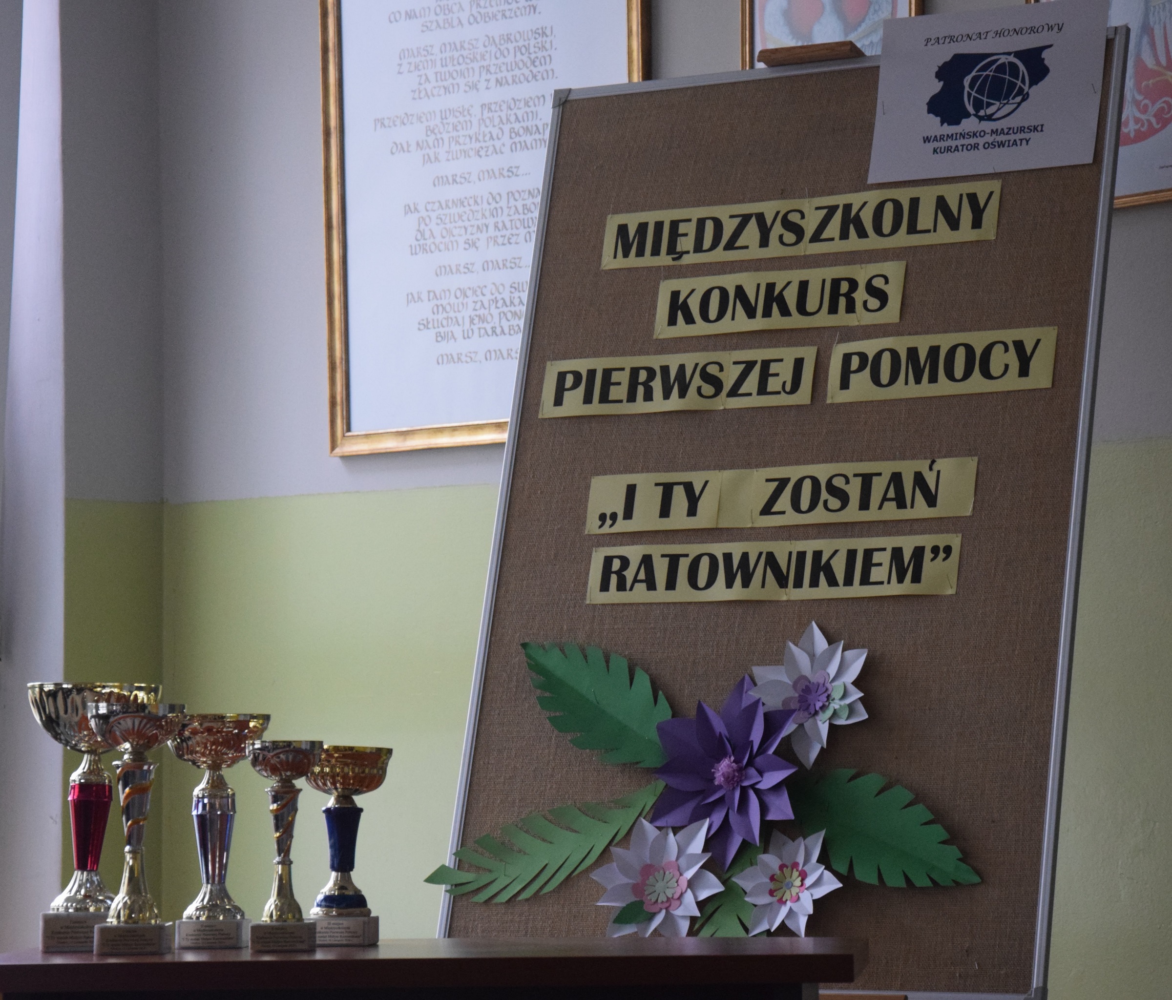 Na stole stoją puchary dla laureatów Konkursu, obok tablica z nazwą konkursu