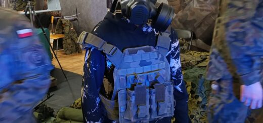 Na zdjęciu znajduje się postać ludzka w masce przeciwgazowej, w tle baner wojskowy.