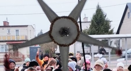 Grupa dzieci idzie w pochodzie kolędników . niosą ze sobą gwiazdę , symbol kolędników.